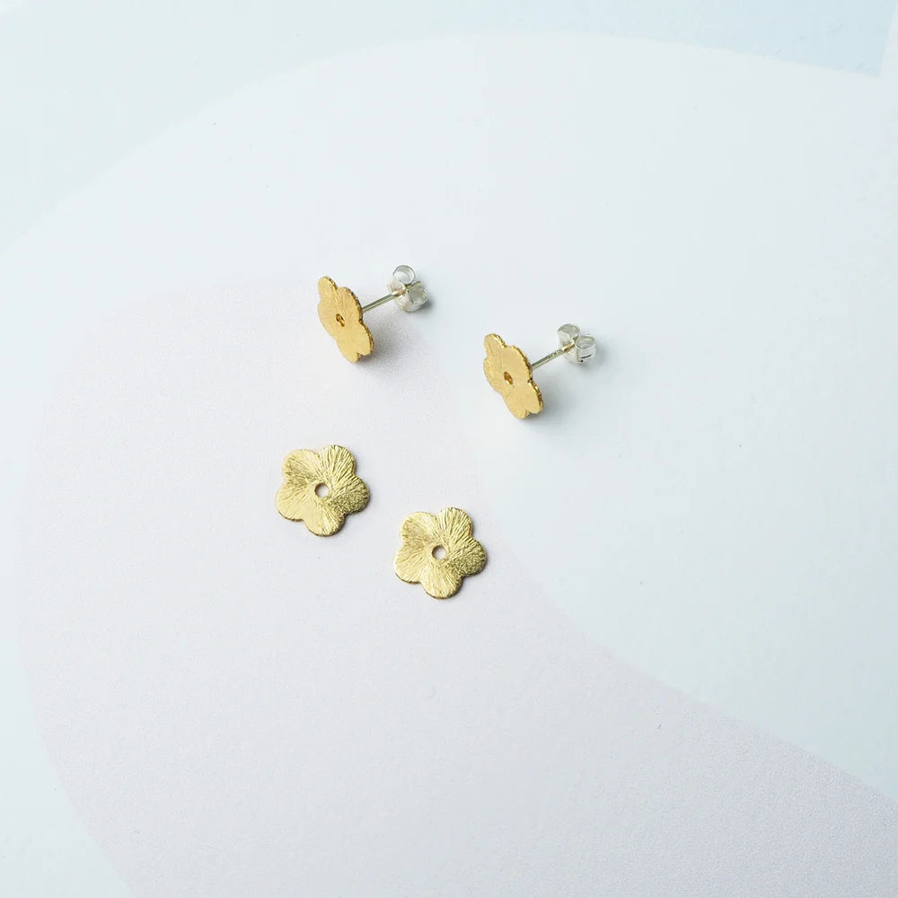 Pair of gold toned flower earring studs with sterling silver posts and sterling silver scroll earring backs next to gold toned flower studs lying flat against a background 