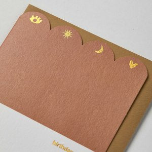 Greetings card top half is dusty rose coloured with a scalloped edge across the top with gold foil icons in the scallops the bottom half is white birthday magic in gold foil letters with dark mustard coloured envelope 