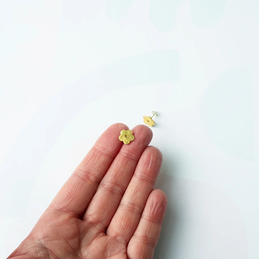 Gold toned flower stud earring held on persons hand next to a matching flower earring with a sterling silver post and back