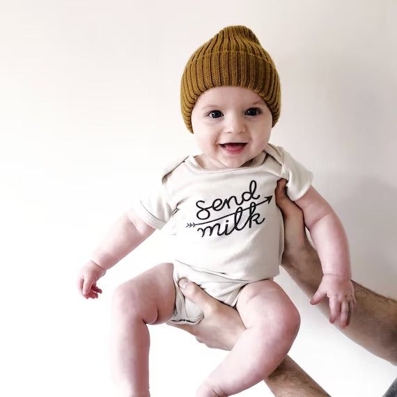 Image of a being held wearing a cream vest with send milk and an arrow printed in black